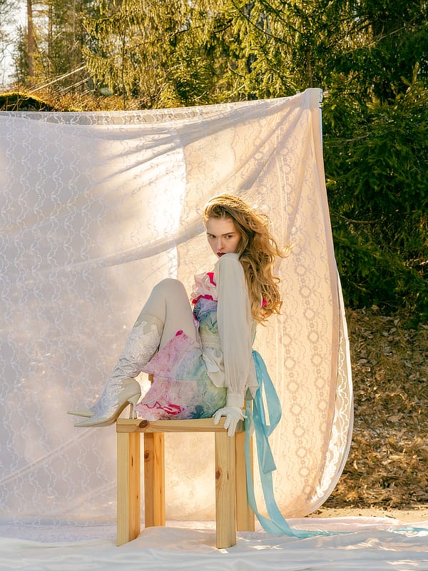 KOE graduate look photographed outdoors on a wooden stool